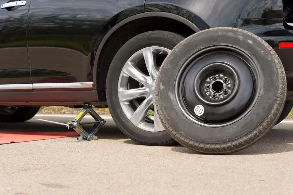 Hands carefully unscrewing a retention bolt to remove a spare tire from a trunk.