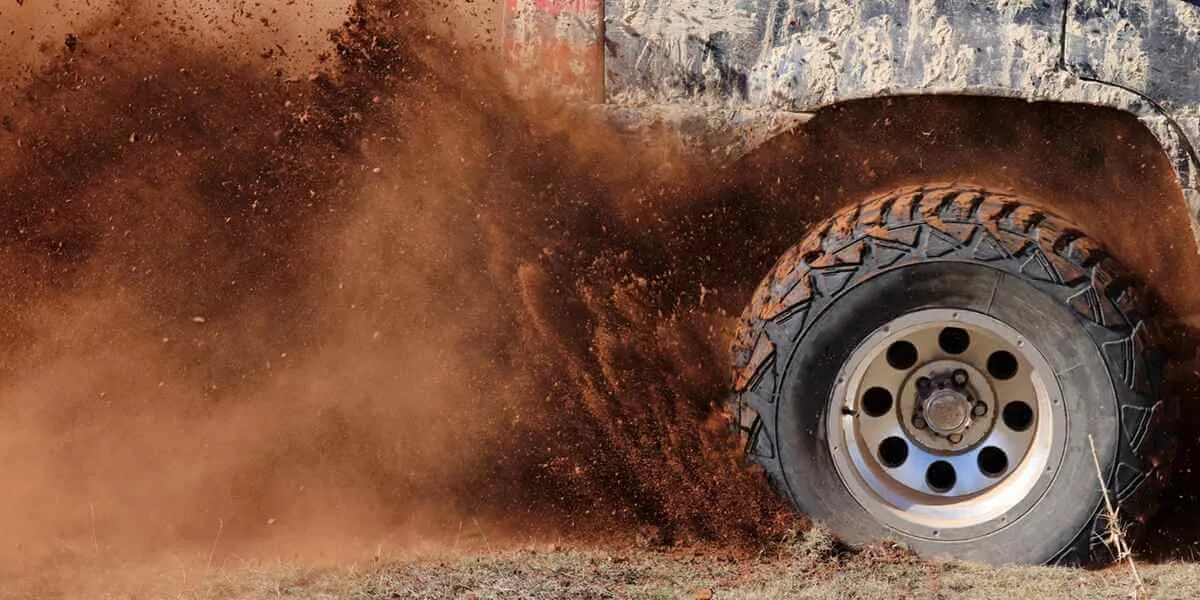 A mechanic checking the clearance of oversized mud tires for proper vehicle fitment.