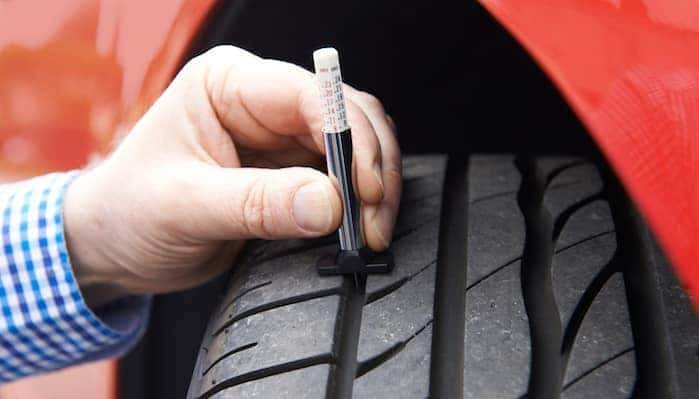 A mechanic uses a professional gauge to measure the tread on a car tire.