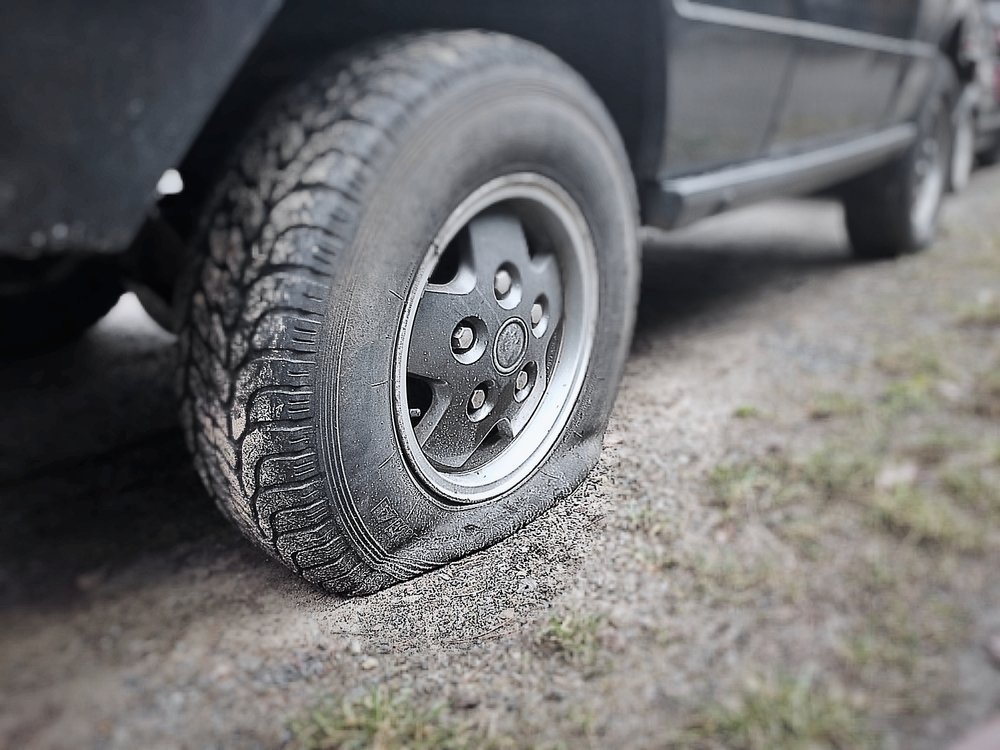 A sharp metal nail embedded in a car tire on an asphalt road.